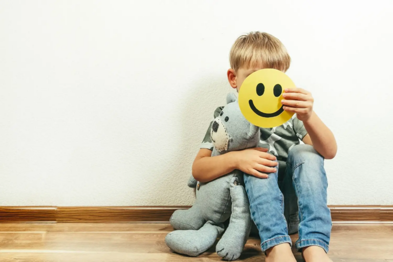 Dziecko trzymające misia, zasłaniające twarz emotikoną uśmiechu